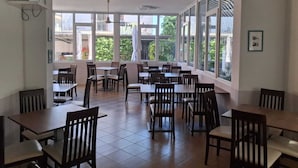 A restaurant with large windows, wooden tables and chairs, and a tiled floor. - Hotel Conca d'Oro (Rimini)