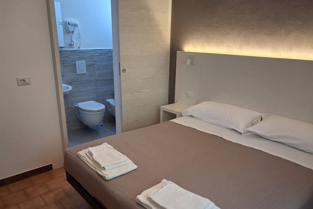 A hotel room with a bed, two towels, a nightstand, and a bathroom visible through an open door.