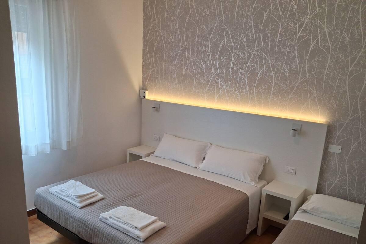 A hotel room with a large bed, two bedside tables, and a wall with a tree pattern.