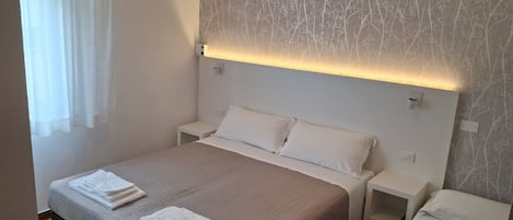 A hotel room with a large bed, two bedside tables, and a wall with a tree pattern.