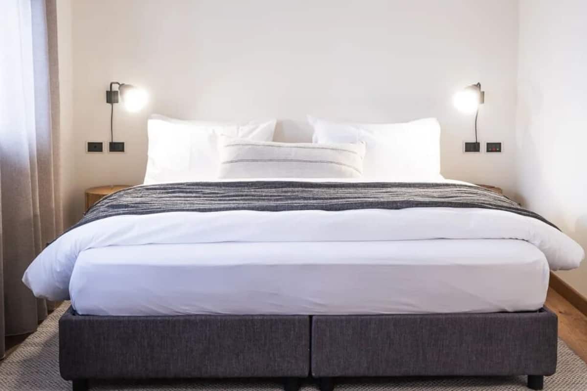 Quarto de hotel moderno com uma cama grande, duas mesas de cabeceira e luminárias fixadas na parede.