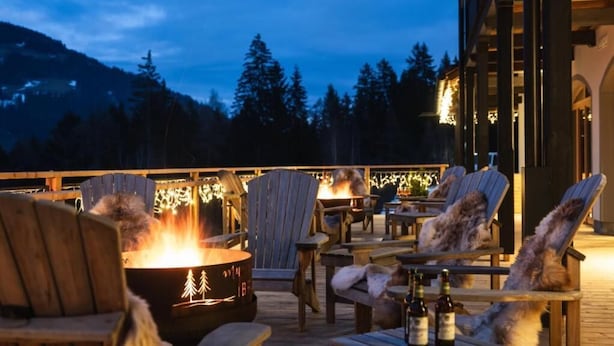 Een gezellig buiten zitgedeelte met houten stoelen en tafels, een vuurkorf en flessen wijn.