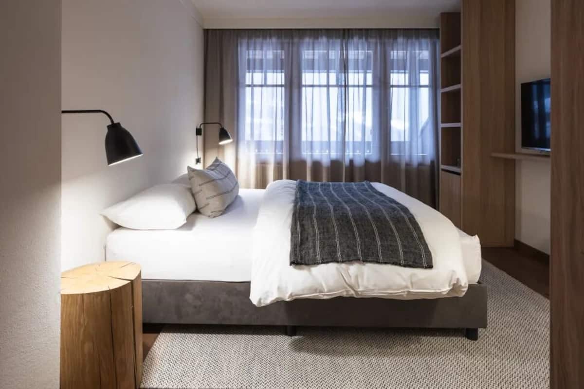 Um quarto moderno com cama, luminárias de cabeceira, televisão e janela com cortinas.