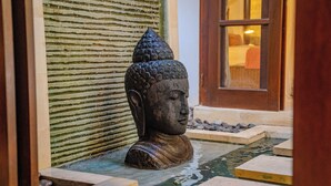A Buddha statue in a water feature, with a textured wall and a wooden door in the background.
