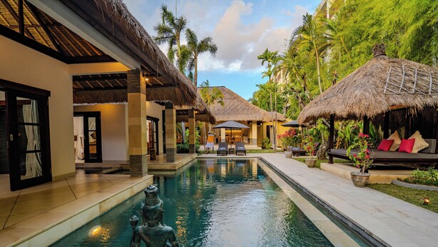 A pool area with a statue, thatched-roof structures, and outdoor seating.