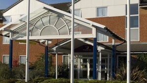 A hotel with a covered entrance, a clock tower, and three flags. - Premier Inn Middlesbrough Central - James Cook Hospital (Middlesbrough)