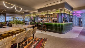 Un área de bar moderna con una barra verde, taburetes y plantas en macetas.