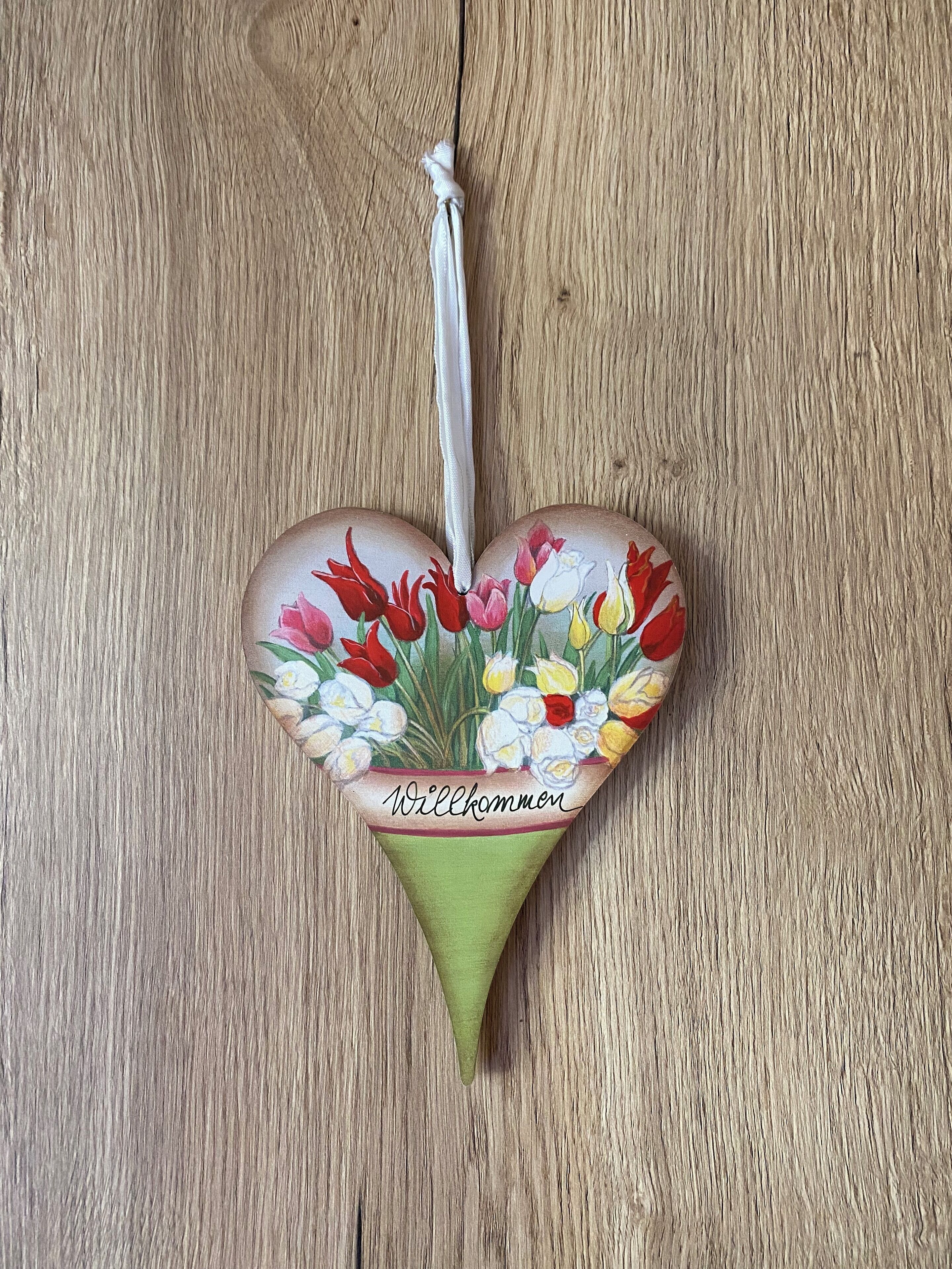 A heart-shaped decoration with a floral design and the word "Willkommen" on a wooden surface.