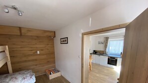 Ein gemütlicher Raum mit Holzboden, einem Bett mit floralem Bettbezug, einer kleinen Holzschatulle und einer Holztür zu einer Küchenzeile mit Fenster.