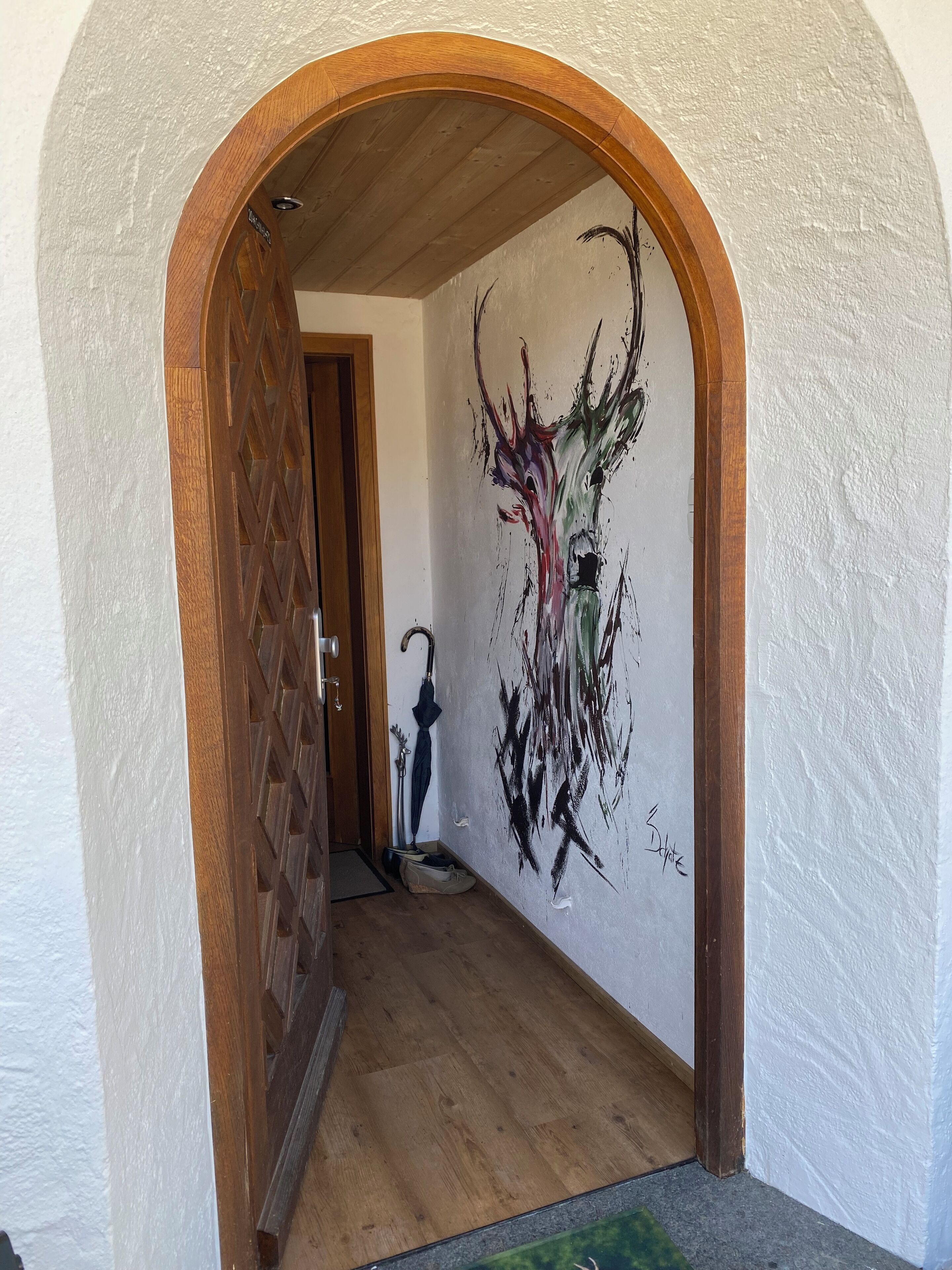 Un couloir avec une porte en bois, un mur orné d’œuvres d’art abstraites et un plancher en bois.