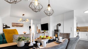 A modern living room with a dining area, a fireplace, and a kitchen in the background. - Fischers Koje in the North Sea resort - with sauna, parking and WLAN (Büsum)