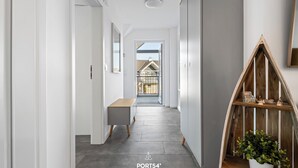 A modern hallway with a wooden bench, a potted plant, and a view of a house through an open door. - Fischers Koje in the North Sea resort - with sauna, parking and WLAN (Büsum)