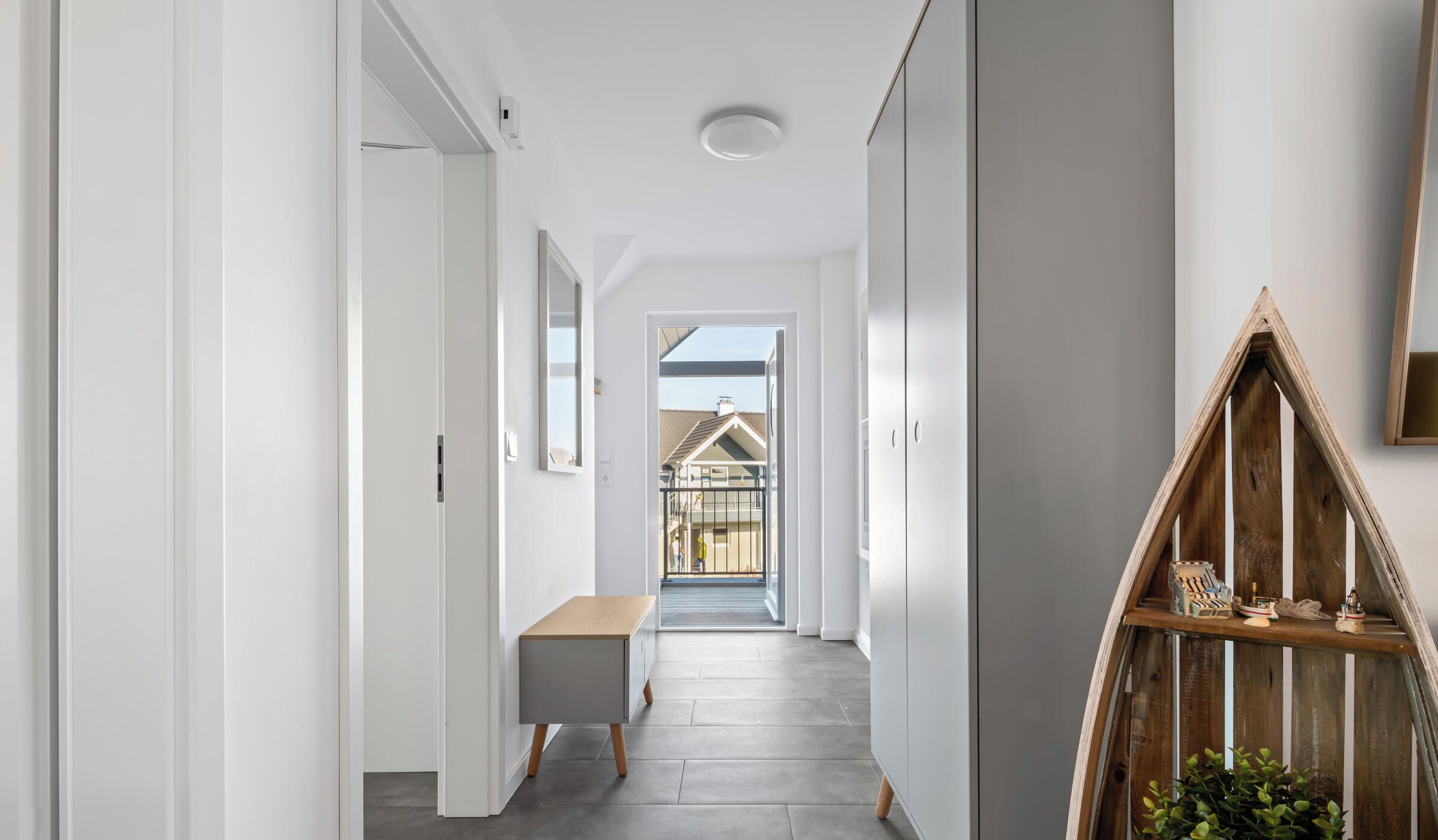 A modern hallway with a wooden bench, a potted plant, and a view of a house through an open door.