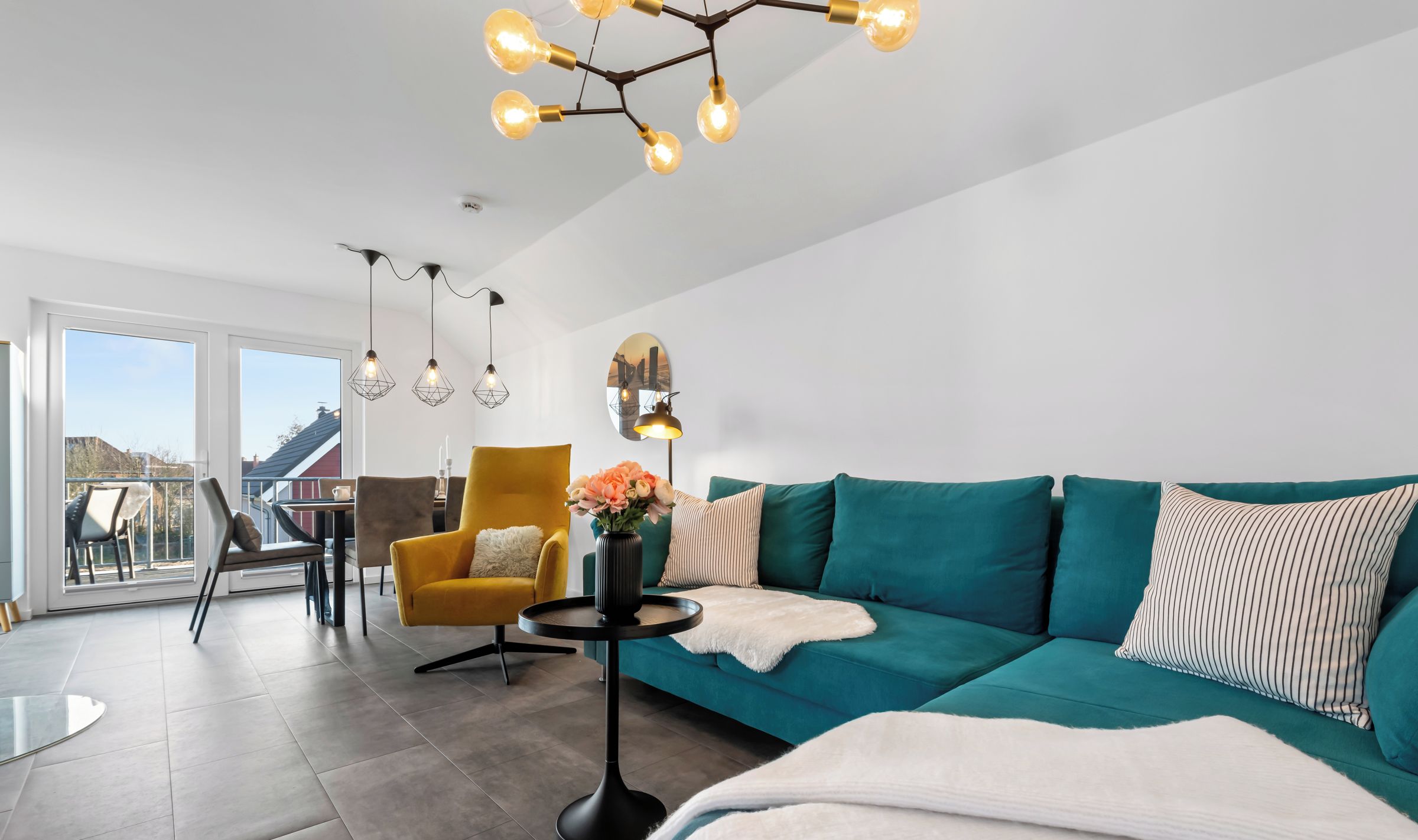 Ein modernes Wohnzimmer mit einem türkisfarbenen Sofa, einem gelben Sessel und einem runden Tisch mit einer Blumenvase.