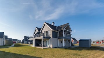 Een modern huis met twee verdiepingen, een balkon, een overdekte patio en een kleine schuur.