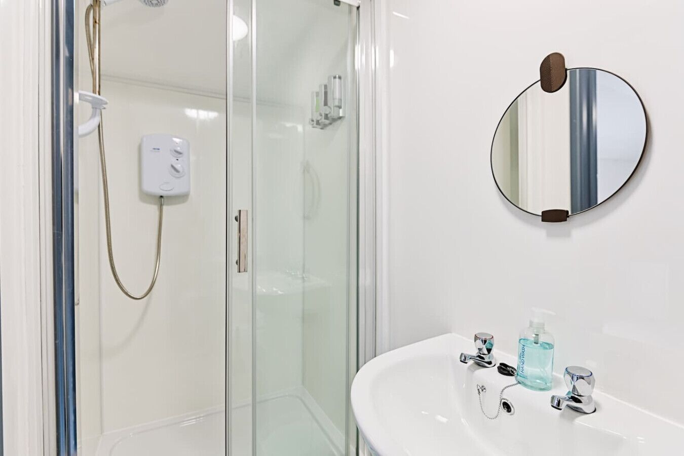 A modern bathroom with a glass shower enclosure, a white sink with a mirror, and a handheld showerhead.