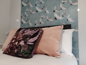 A bed with a floral pillow, a peach-colored pillow, and a white pillow.