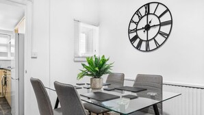 A modern meeting room with a glass table, grey chairs, a potted plant, and a large black clock on the wall.