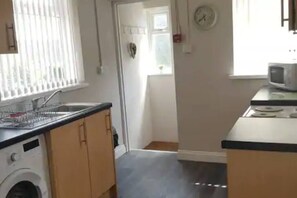 Compact kitchen area with microwave, sink, and washing machine for basic cooking and laundry needs.