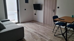 Een kamer met een bank, een tafel met stoelen, een aan de muur bevestigde televisie en een schuifdeur.