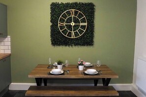 A dining area with a table for four, featuring a decorative clock and a potted plant.