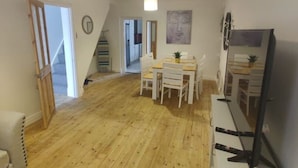 A spacious room with a wooden floor, a dining table with chairs, a TV, and a staircase leading to another level. - 3 Bed • Parking • Smart TV`s • Great for Work (Clydach)