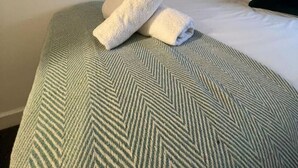 A neatly made bed with a green and white herringbone patterned bedspread, two rolled towels, and two pillows. - 3 Bed • Parking • Smart TV`s • Great for Work (Clydach)
