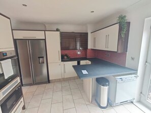 A kitchen with a refrigerator, oven, and a small trash bin.