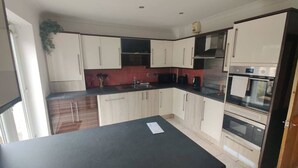 A kitchen with white cabinets, a black countertop, and a red backsplash. - 3 Bed • Parking • Smart TV`s • Great for Work (Clydach)