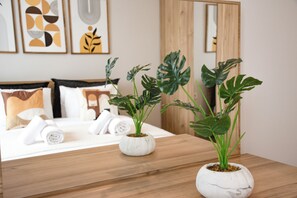 Ein Hotelzimmer mit einem Bett, zwei Topfpflanzen, einem Nachttisch aus Holz und Kunstwerken an der Wand.