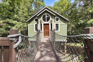 A wooden bridge leading to a green building with a wooden door and two windows. - Sanctuary Treehouse with Jacuzzi (Eureka Springs)