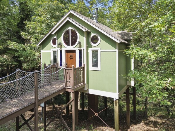A wooden treehouse with a rope bridge, surrounded by trees. - Sanctuary Treehouse with Jacuzzi (Eureka Springs)