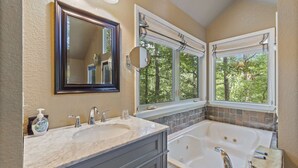 A bathroom with two sinks, a large bathtub, a mirror, and windows with curtains. - Royal Oak Treehouse with Jacuzzi (Eureka Springs)