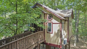 A treehouse with a wooden deck, a small window, and a circular window on the side. - Royal Oak Treehouse with Jacuzzi (Eureka Springs)