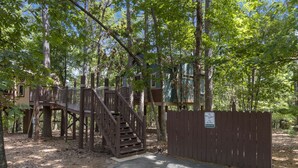 Una estructura tipo casa del árbol con escaleras de madera y una entrada cercada.