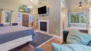 Un dormitorio con cama, chimenea, televisión y ventana con vistas a árboles.