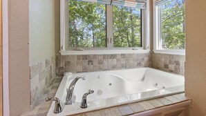 Un baño con una bañera grande, dos ventanas con persianas y un salpicadero de azulejos.