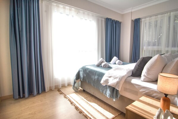 A bedroom with a bed, a bedside table with a lamp, and a window with curtains.