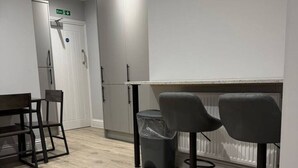 A modern kitchen with a wooden floor, a dining table with chairs, a trash bin, and a refrigerator. - Contractor Stay • 2 Bed • 2 En-suites (Swansea)