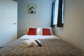 A hotel room with a bed, a remote control, and a rolled towel on the bed.