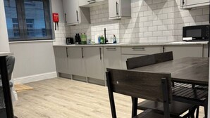 A modern kitchen with white cabinets, a black range hood, and a dining area with a table and chairs. - Contractor Stay • 2 Bed • 2 En-suites (Swansea)