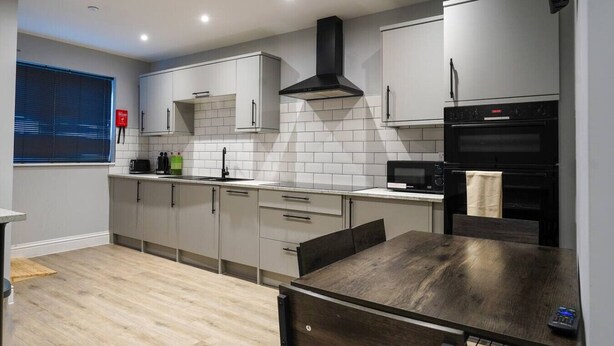 A modern kitchen with white cabinets, a black range hood, and a microwave. - Contractor Stay • 2 Bed • 2 En-suites (Swansea)