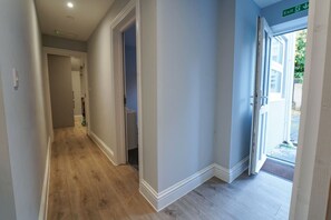 A hallway with wooden flooring, white walls, and a door leading outside.