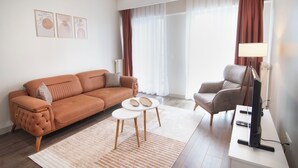 Una sala moderna con un sofá, una butaca, una mesita de centro, un televisor de pantalla plana y una lámpara.