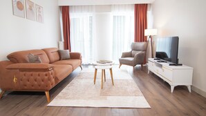 Una sala de estar moderna con un sofá, un sillón, un mueble para televisión y un ventanal con cortinas.
