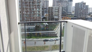 Un balcón con vistas a edificios altos, barandilla de vidrio y piso de baldosas.