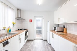 Una cocina compacta con armarios blancos, un microondas, una estufa y un lavabo.