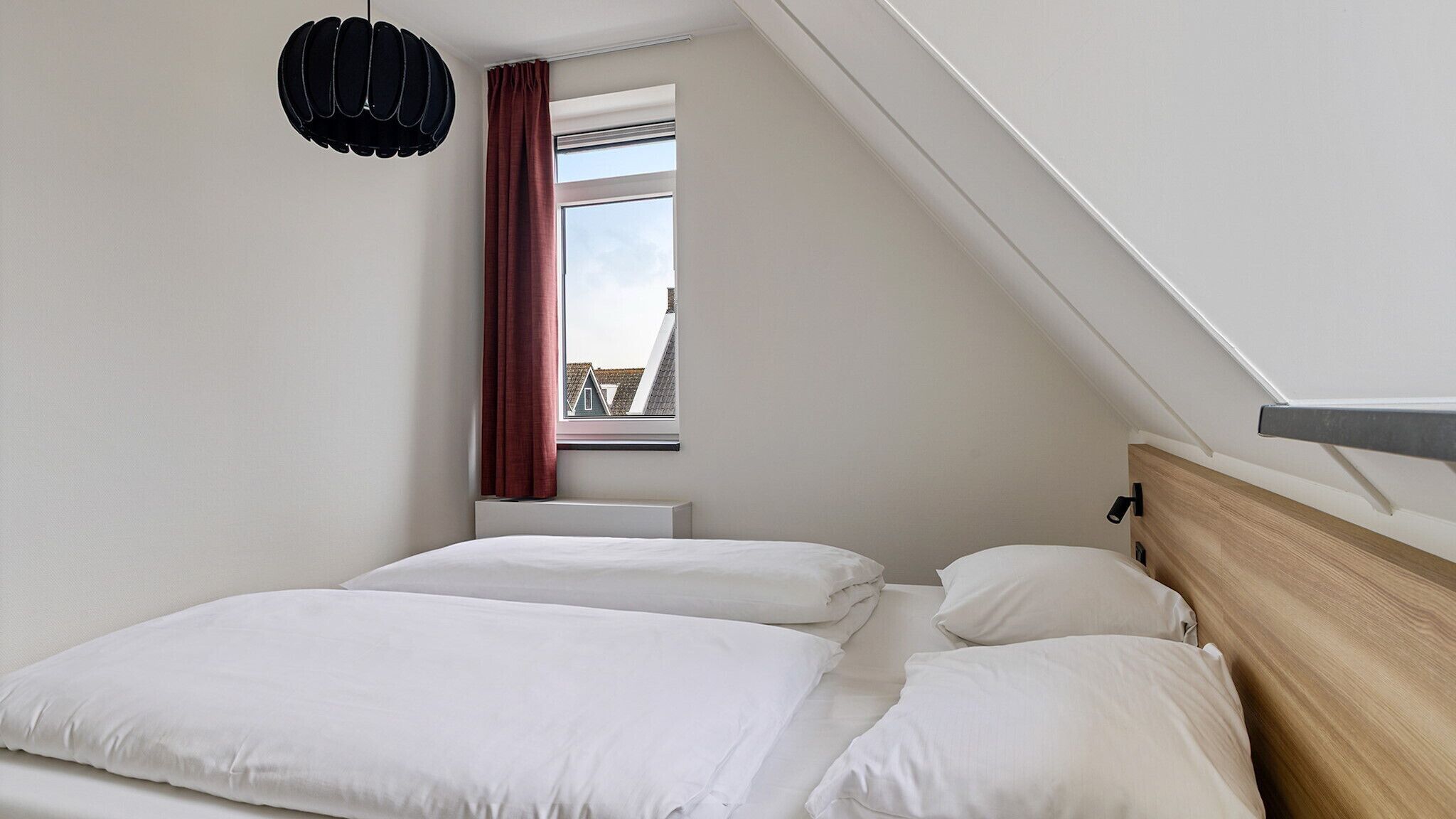 Quarto com cama, janela com cortinas, luminária pendente e teto inclinado.