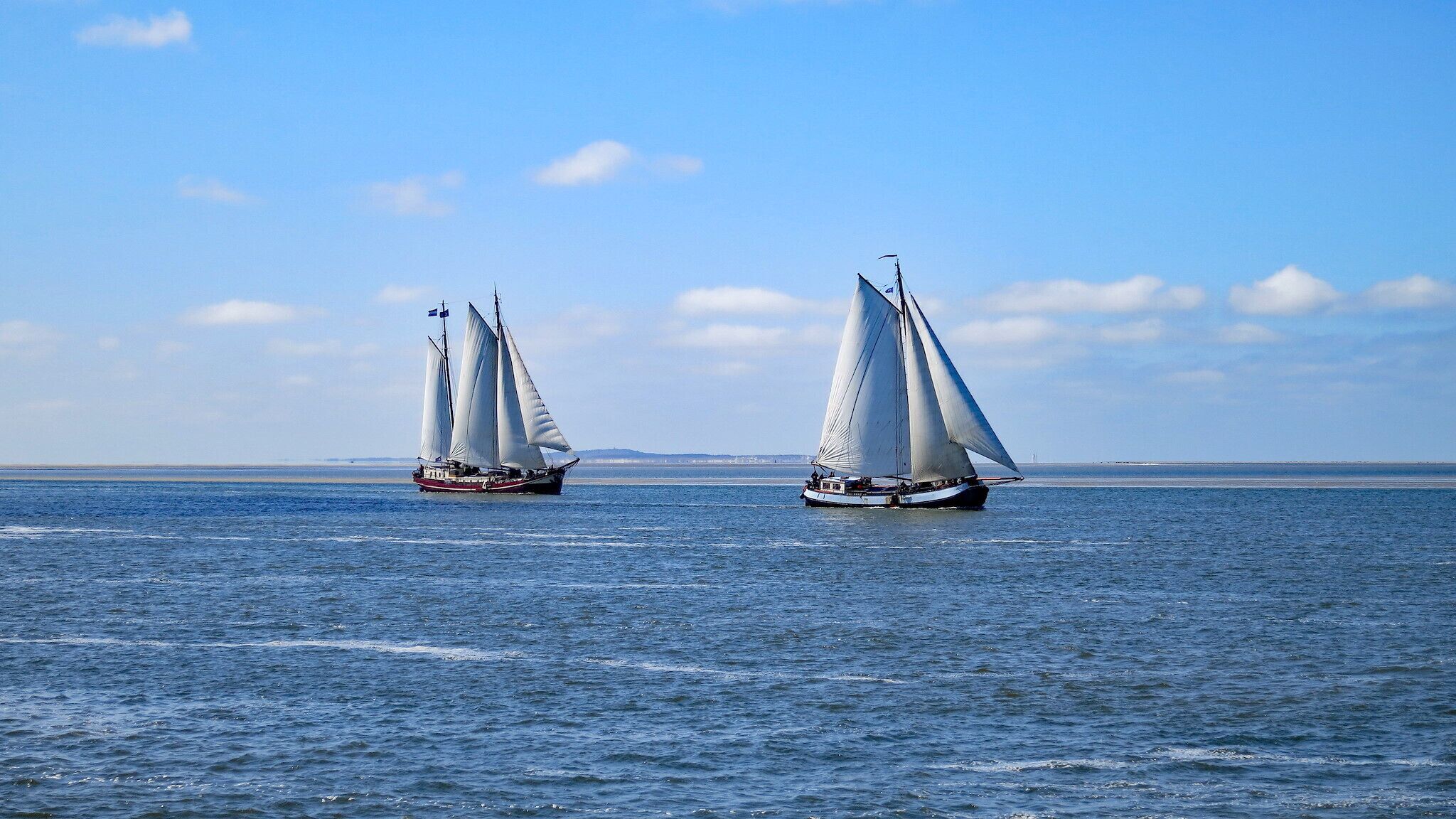 Zwei Segelboote auf ruhiger See unter klarem Himmel.