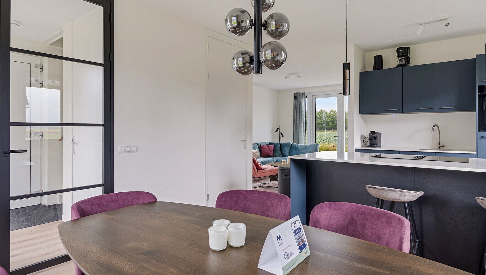 A modern kitchen with dark cabinets, a central island, and a dining area with a wooden table and purple chairs.
